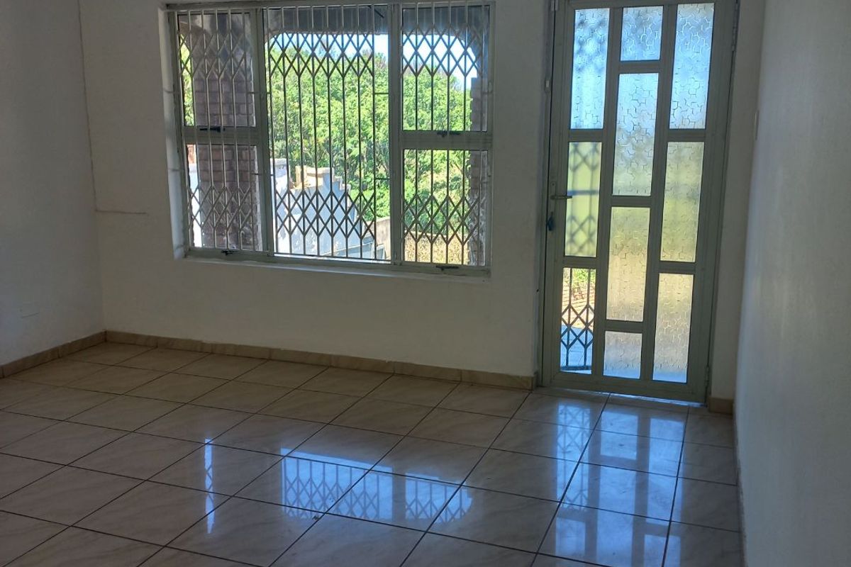 An empty living area featuring neutral tiled flooring, a glass panel door, and security bars on the windows, offering a clean, blank canvas.