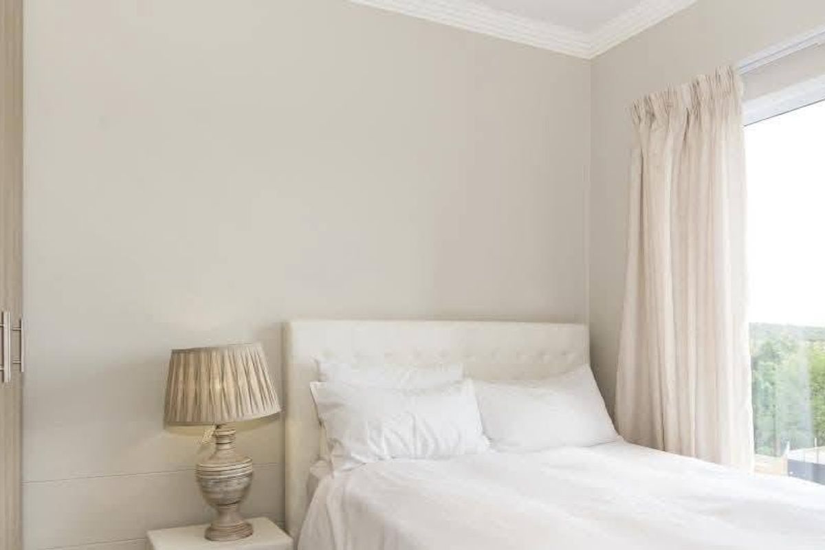 A bright bedroom featuring built-in light wood cabinetry, crown molding, and large windows providing natural light and exterior views.