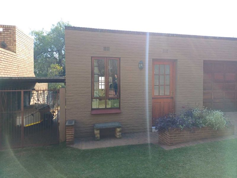 Rear view of the cottage featuring a brick facade, timber framed door and window, paved patio area, and a built-in brick planter box.