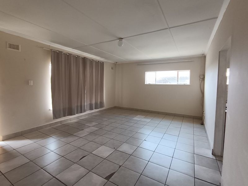 An empty living room featuring tiled flooring, neutral walls, and natural light from windows, providing a blank canvas for interior design.