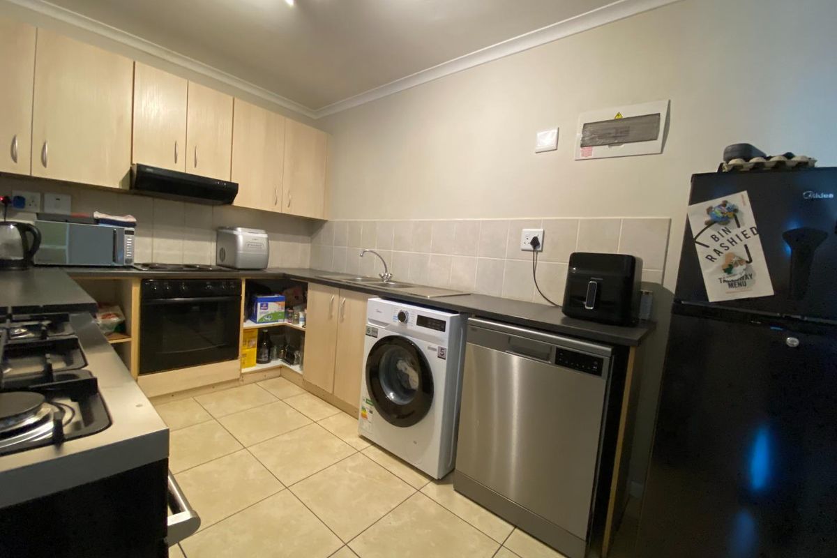 Functional kitchen featuring light wood cabinetry, tiled splashback, integrated oven, hob, extractor fan, and dedicated space for laundry and dishwasher appliances.