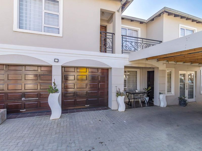 Front elevation of a double-story home featuring a double garage, paved driveway, covered carport, and an upper-level balcony with wrought iron railings.