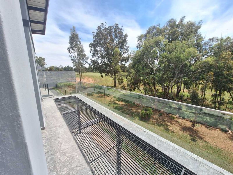 A modern balcony featuring a sleek glass balustrade and metal grate flooring, offering an elevated view of the surrounding trees and landscape.