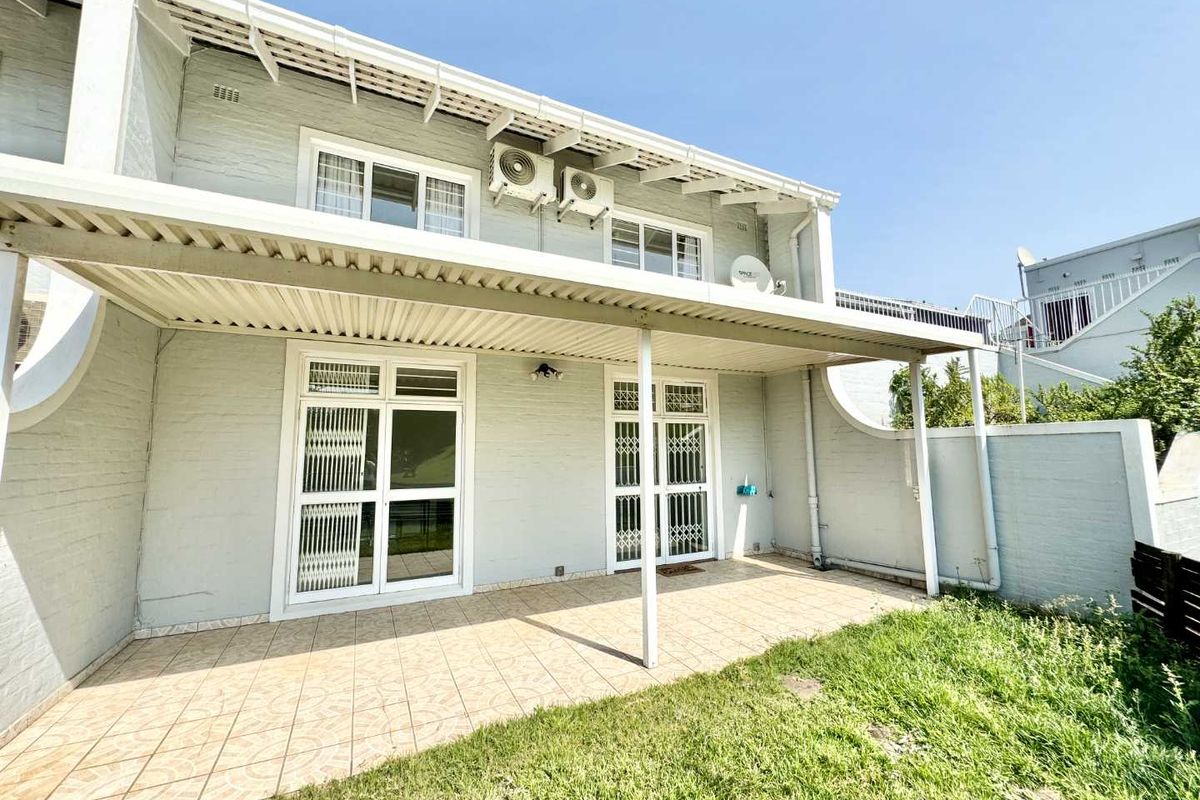 Rear exterior view of the townhouse featuring a covered tiled patio, security gates, and wall-mounted air conditioning units.
