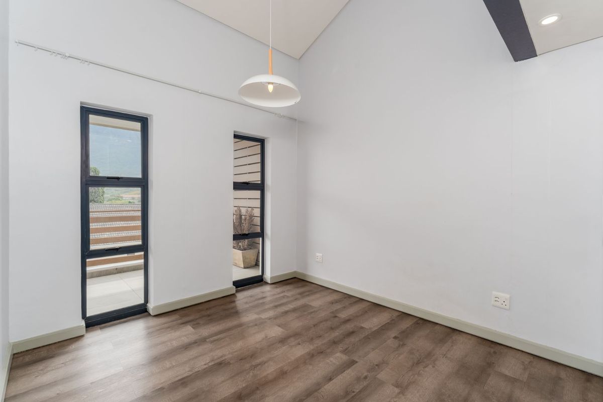A bright, empty bedroom featuring high vaulted ceilings, modern wood-look flooring, and dual access points to an outdoor balcony area.