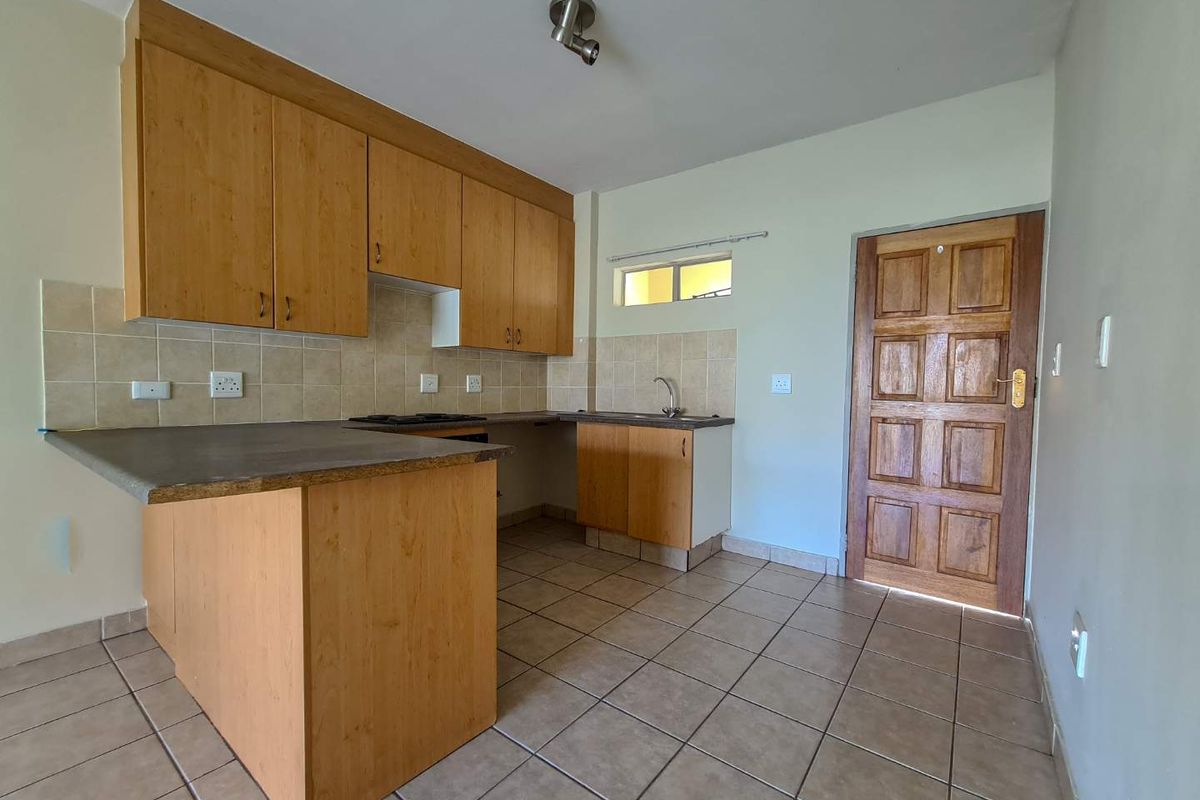 A functional kitchen featuring light wood laminate cabinetry, tiled backsplash, ceramic flooring, and a built-in hob, presented in a clean, vacant state.