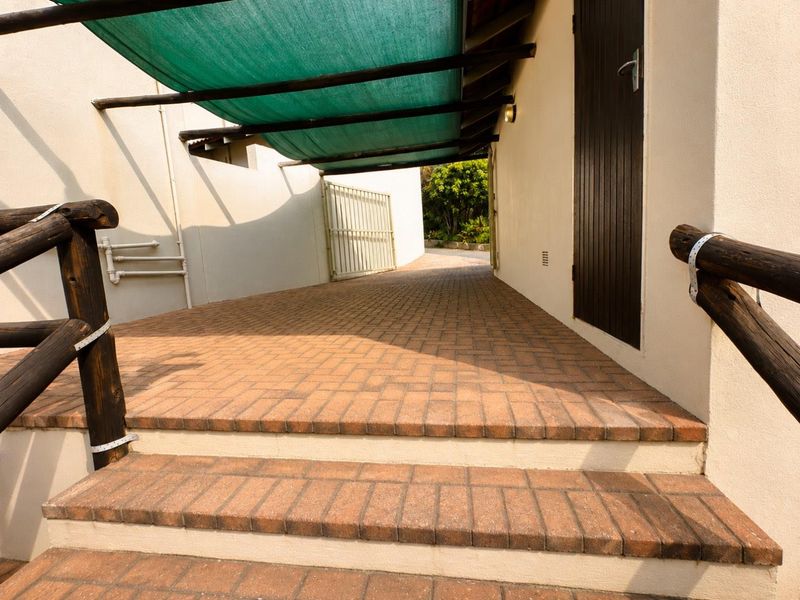 A paved outdoor walkway featuring a shade cloth canopy, timber handrails, and access to an external door.
