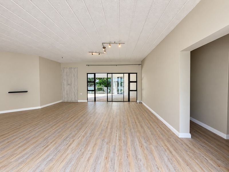 A spacious, empty living room featuring modern laminate flooring, neutral walls, a built-in cupboard, and large sliding glass doors leading to an outdoor area.
