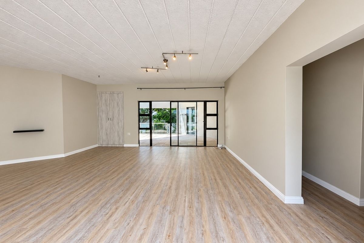 A spacious, empty living room featuring modern laminate flooring, neutral walls, a built-in cupboard, and large sliding glass doors leading to an outdoor area.