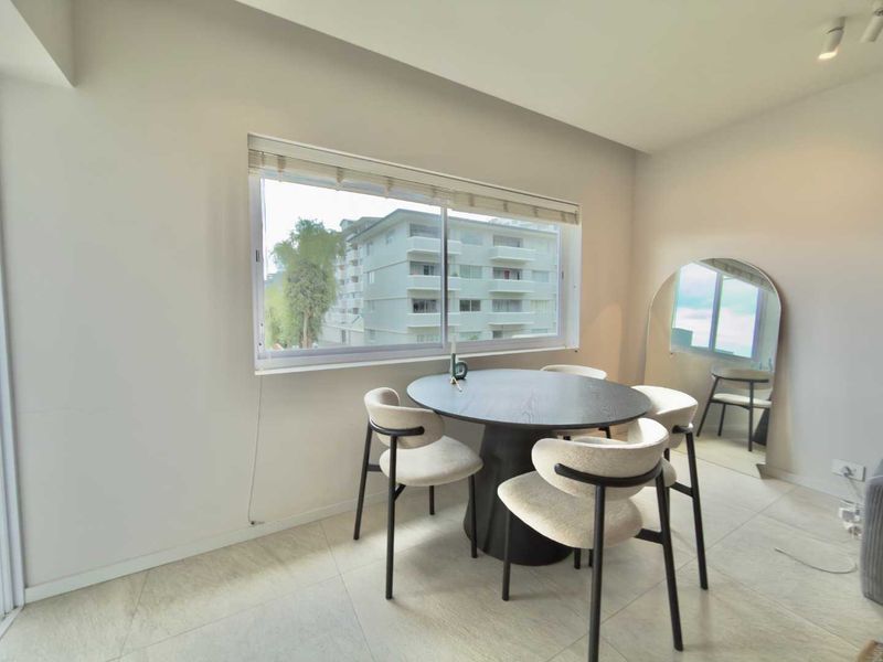 A bright and modern dining area featuring large sliding windows, neutral tiled flooring, and recessed ceiling lighting, offering a clean and contemporary living space.