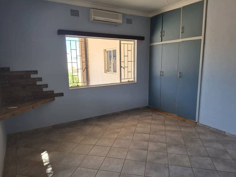 A spacious bedroom featuring built-in cupboards, tiled flooring, an air conditioning unit, and security bars on the windows.