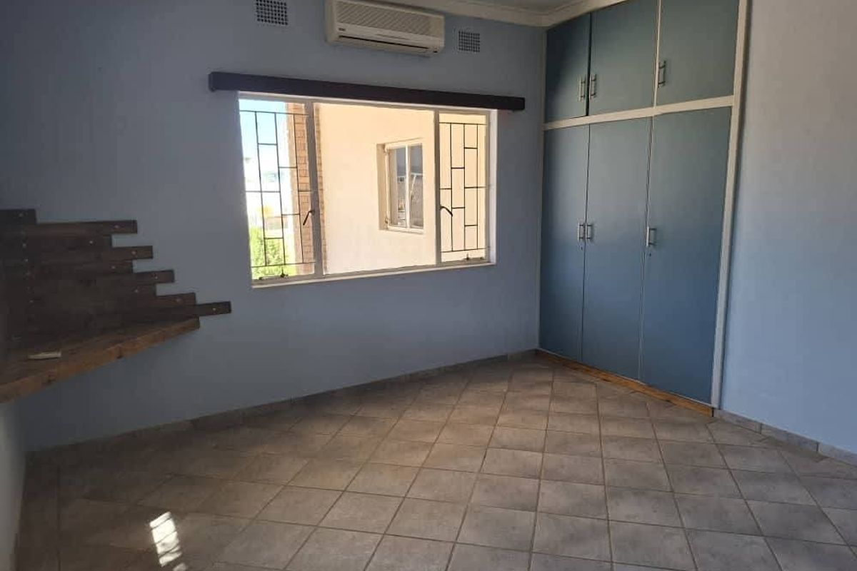 A spacious bedroom featuring built-in cupboards, tiled flooring, an air conditioning unit, and security bars on the windows.