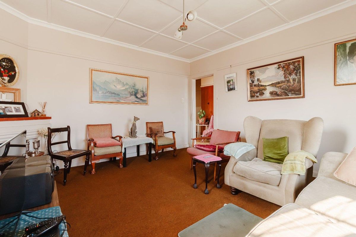 A traditional living room featuring a fireplace, picture rails, and a tiled ceiling, currently finished with dated carpeting.