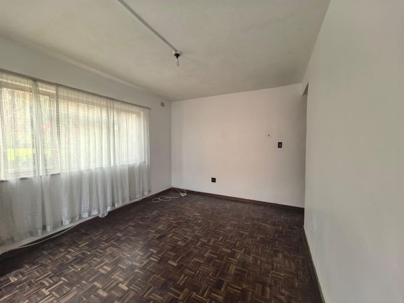 An empty living room featuring original parquet flooring, a large window with curtain tracks, and basic lighting fixtures.