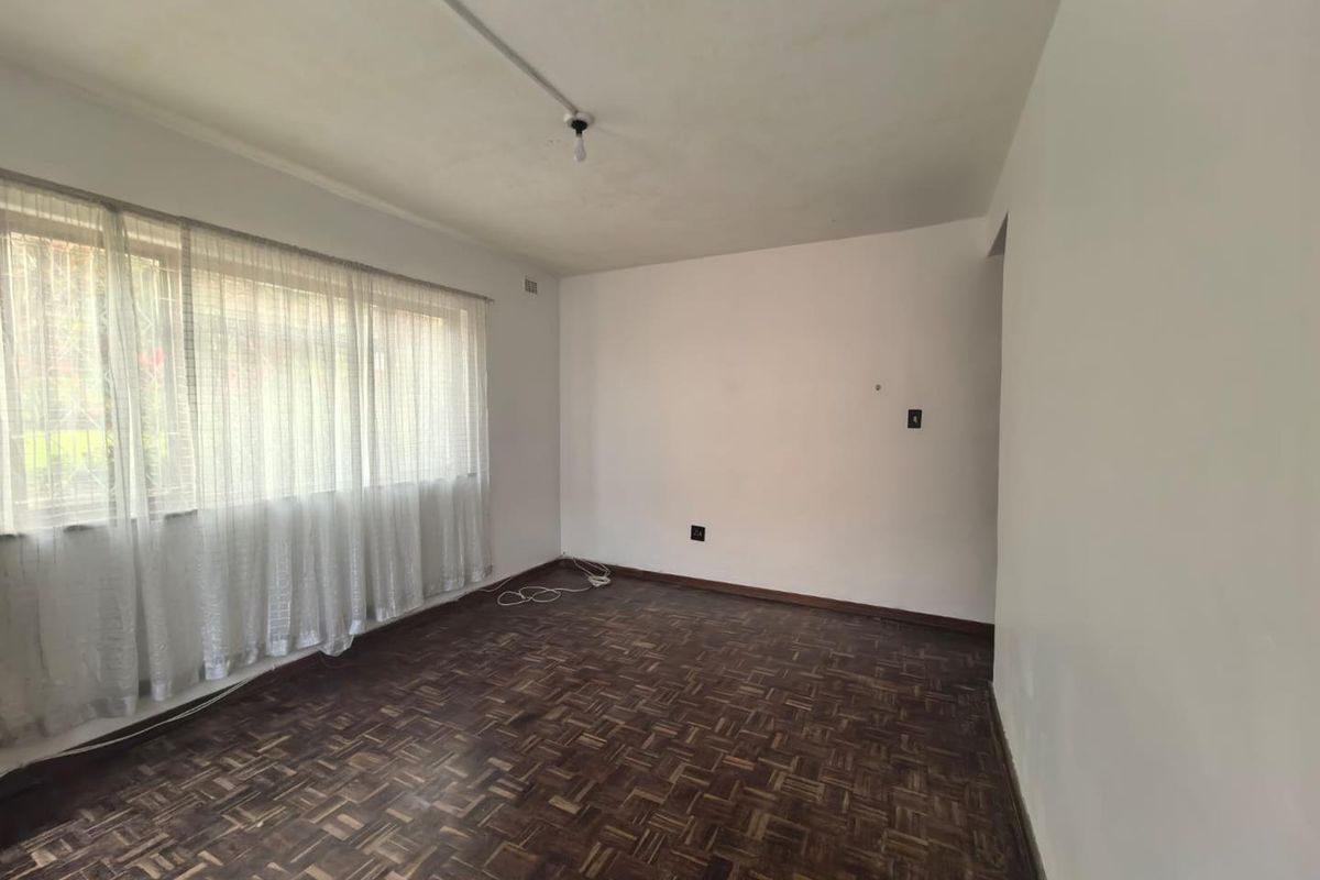 An empty living room featuring original parquet flooring, a large window with curtain tracks, and basic lighting fixtures.