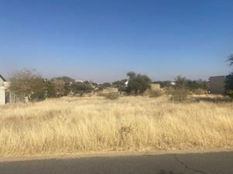 A view of a vacant residential plot of land with dry grass and surrounding neighborhood vegetation.