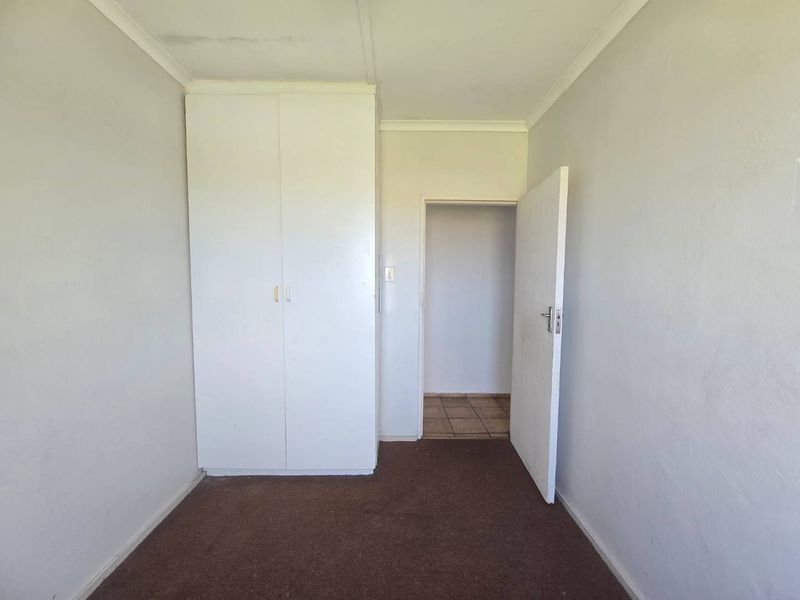 An empty bedroom featuring a built-in wardrobe, carpet flooring, and coving, showing signs of ceiling water staining and general wear.