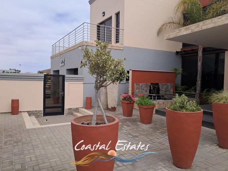 Modern front exterior featuring paved driveway, stone-clad water feature, and a balcony with stainless steel railings.