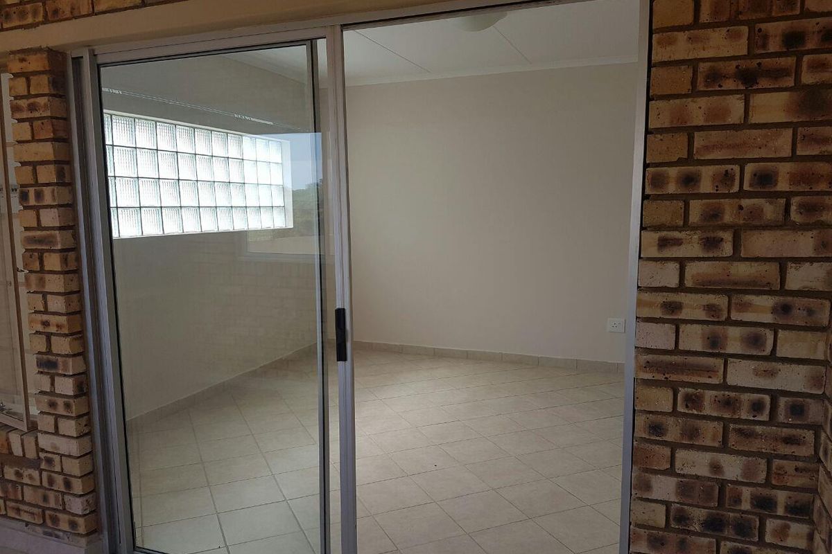 An empty bedroom featuring tiled flooring, a glass block window, and access via a sliding glass door framed by exposed brickwork.