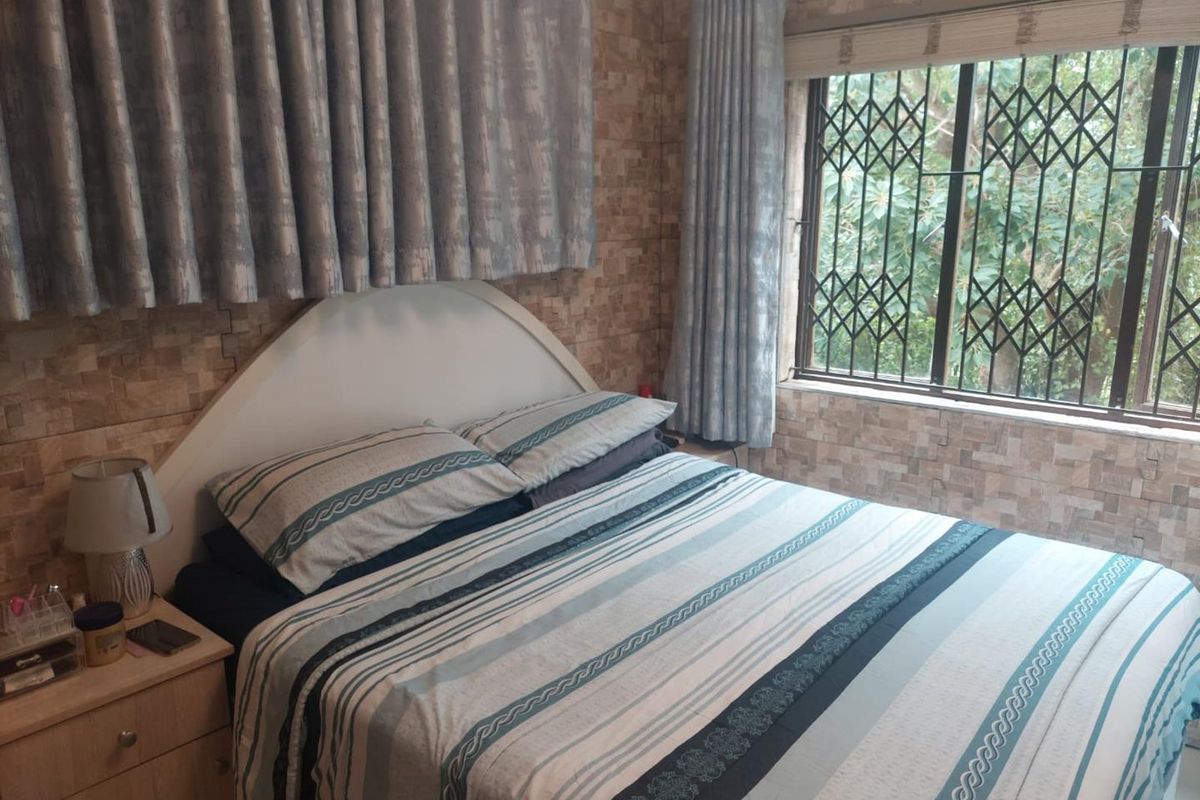 A bedroom featuring textured wall cladding and a window fitted with a security gate.