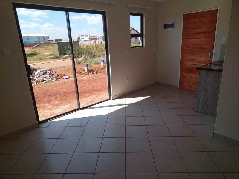 An empty open-plan living area featuring tiled flooring, a sliding glass door leading outdoors, and a partial view of the kitchen cabinetry.