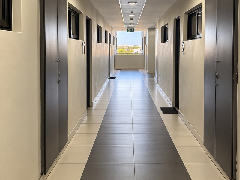 A clean, well-lit apartment hallway featuring modern two-tone tiled flooring, recessed ceiling lights, and integrated storage cupboards along the walls.