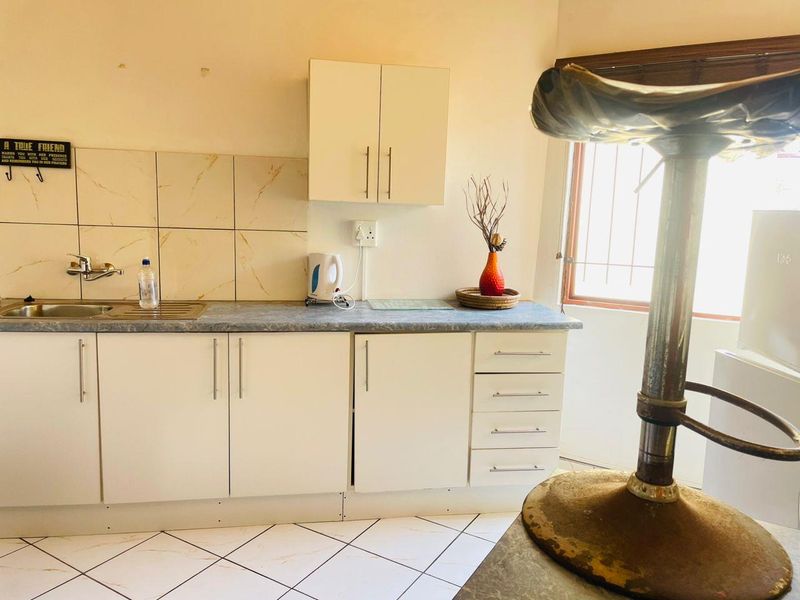 A compact kitchen featuring white built-in cabinetry, a laminate countertop, stainless steel sink, and tiled backsplash with neutral floor tiles.