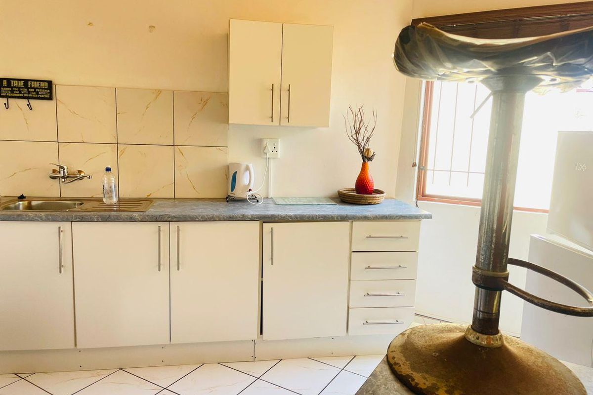 A compact kitchen featuring white built-in cabinetry, a laminate countertop, stainless steel sink, and tiled backsplash with neutral floor tiles.