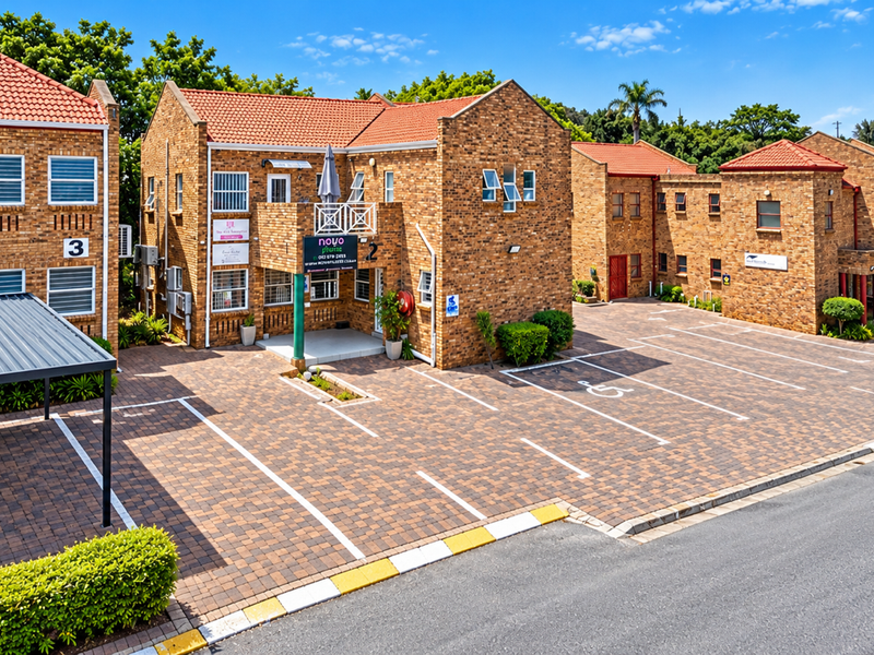 A well-maintained commercial office complex featuring face brick architecture, a paved parking lot with designated bays, and a covered carport.