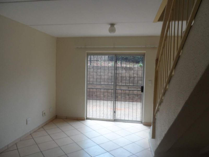 An empty living area featuring tiled flooring, a staircase with a balustrade, and a sliding glass door leading to an outdoor patio area.