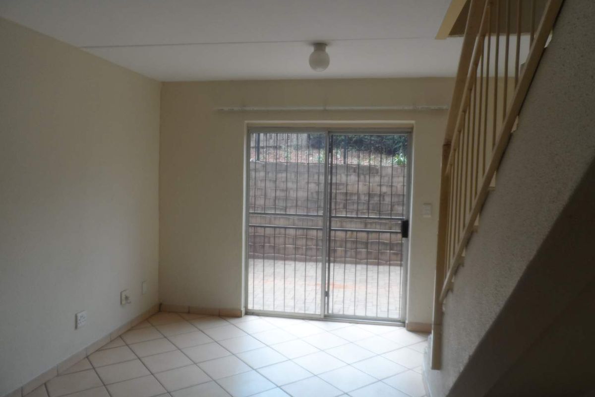 An empty living area featuring tiled flooring, a staircase with a balustrade, and a sliding glass door leading to an outdoor patio area.