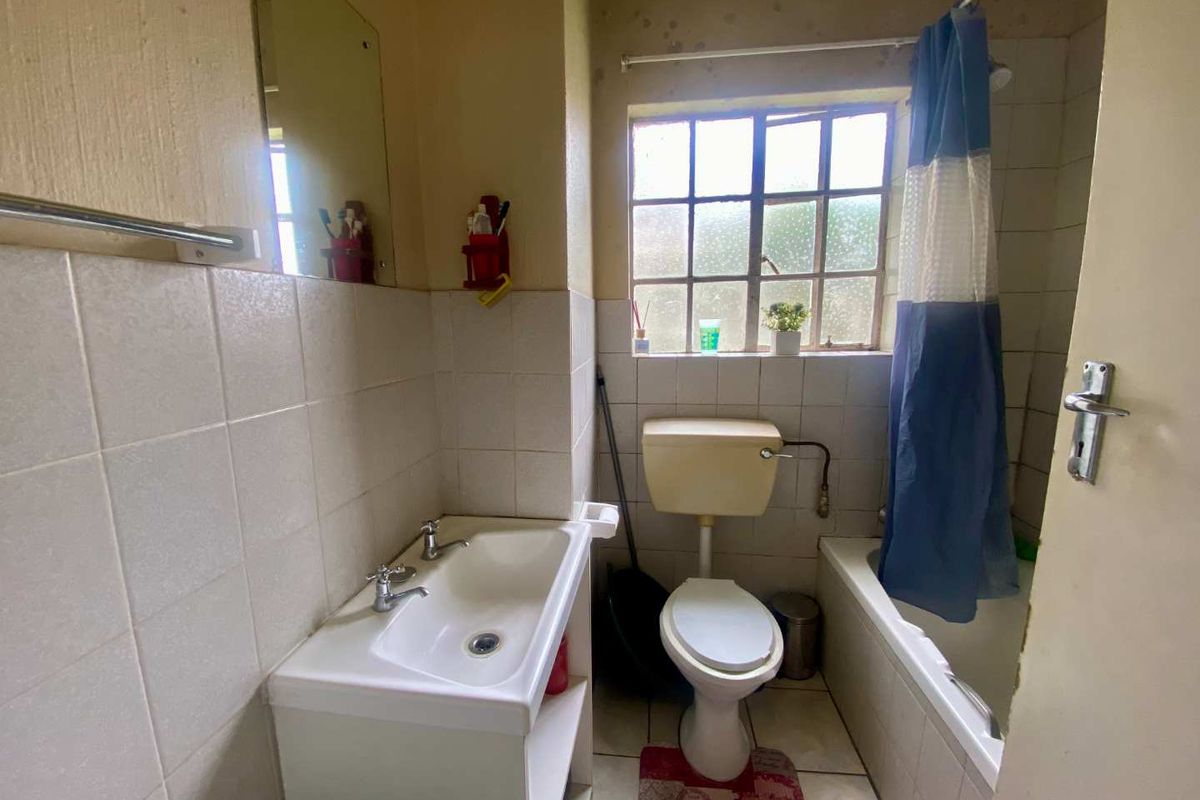 A dated bathroom featuring a standard bathtub, toilet, and vanity basin with tiled walls and a window.