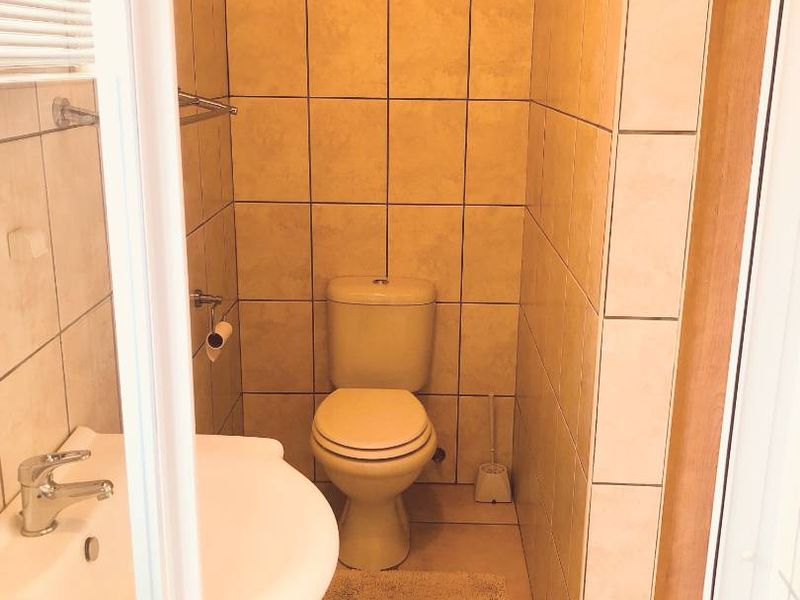 A functional bathroom featuring ceramic wall and floor tiles, a pedestal washbasin, and a standard toilet suite.
