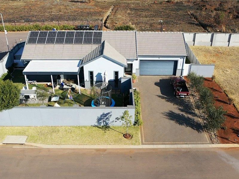 Aerial view of a modern residential property featuring a tiled roof with solar panels, a paved driveway, a garage, and a private enclosed garden.
