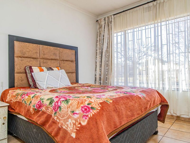 A bedroom featuring tiled flooring, a large window with security bars, and coved ceiling detailing.