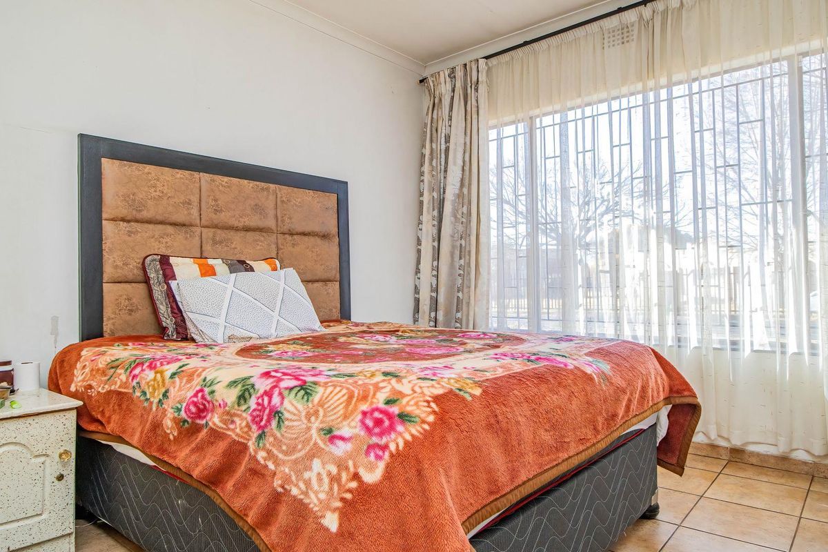 A bedroom featuring tiled flooring, a large window with security bars, and coved ceiling detailing.