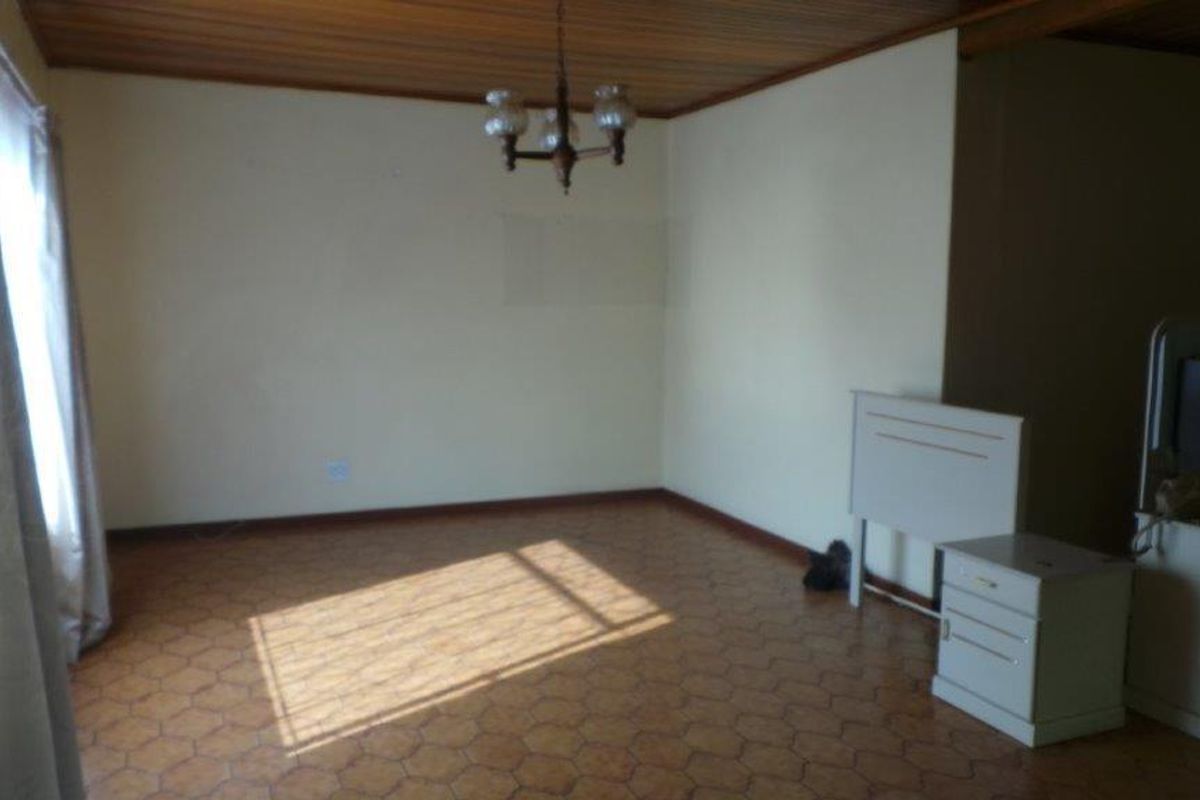A spacious living area featuring a timber-clad ceiling, tiled flooring, and a central pendant light fixture, offering a blank canvas for renovation.