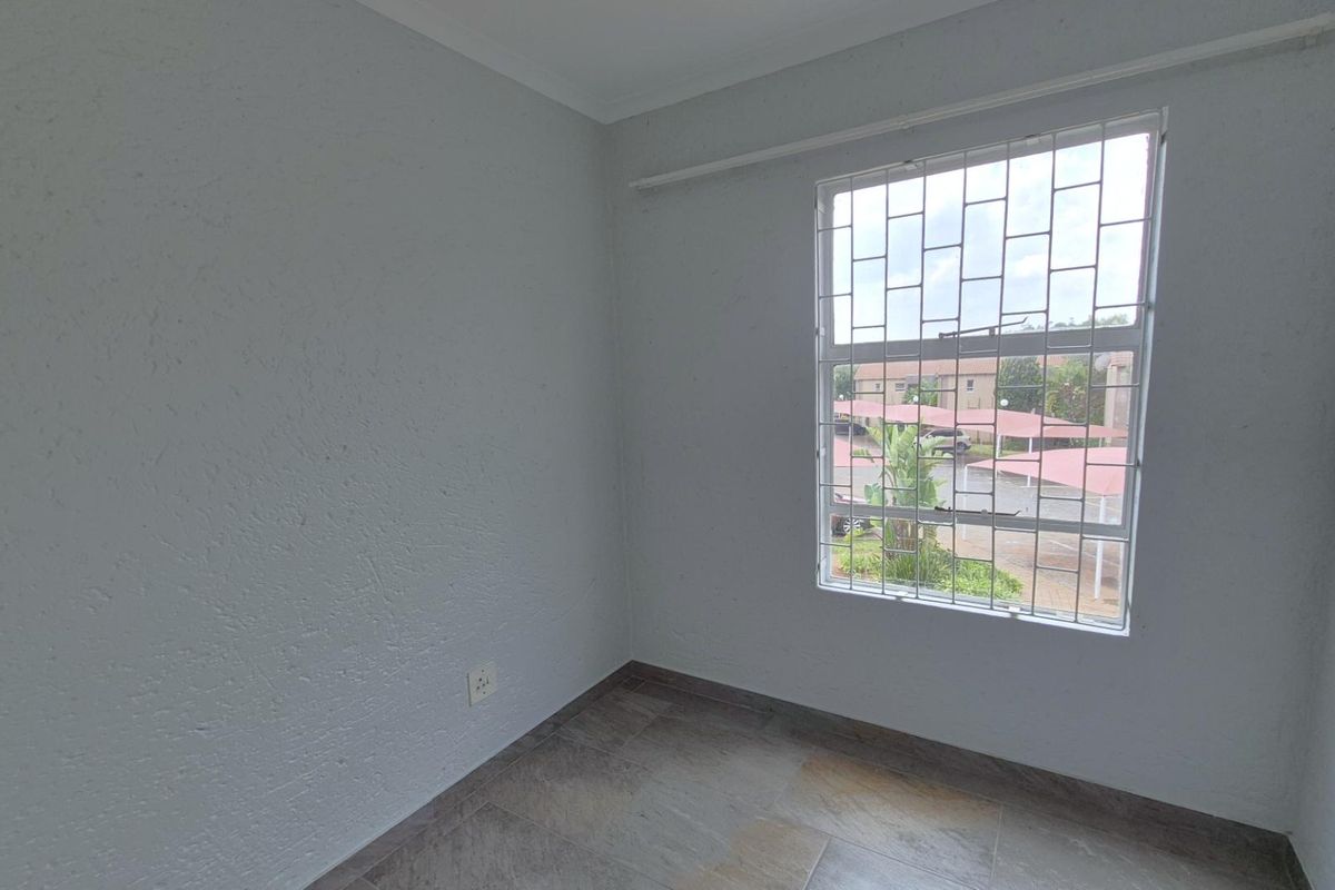 A bright, empty bedroom featuring tiled flooring, textured walls, and a window fitted with security bars.