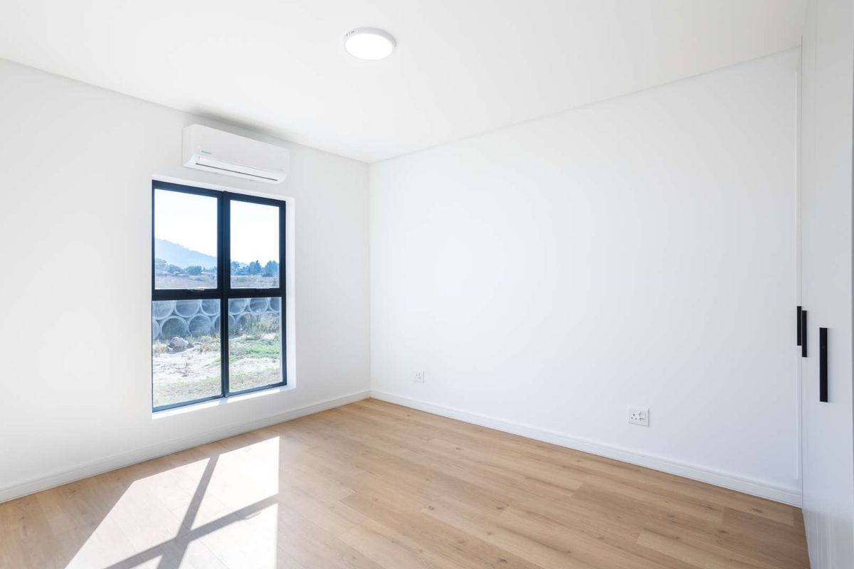A bright, modern bedroom featuring light wood-look flooring, built-in cabinetry, and a wall-mounted air conditioning unit.
