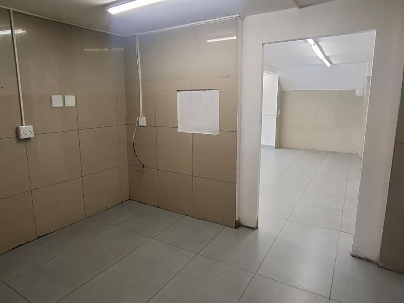 An empty utility or storage space featuring tiled walls and flooring with overhead fluorescent lighting, suitable for various commercial storage or prep purposes.
