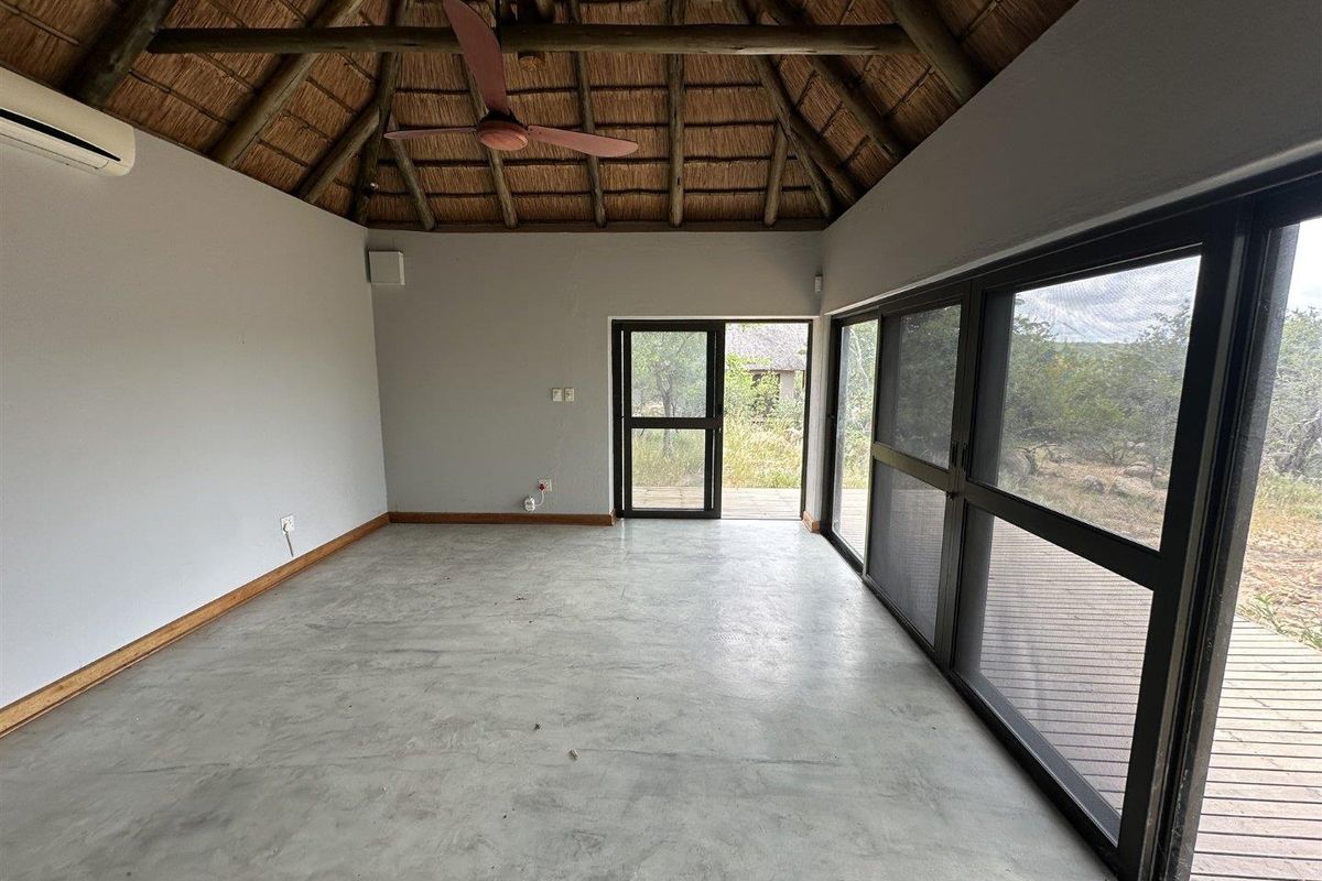 An empty living space featuring a high thatched roof with exposed timber beams, polished concrete floors, and large sliding glass doors leading to a deck.