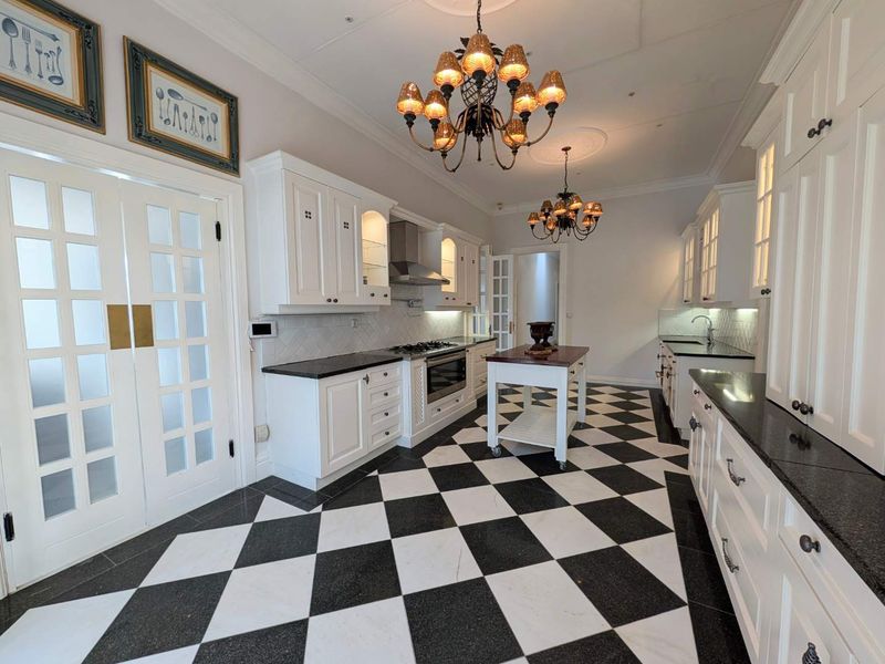 Spacious kitchen featuring classic white cabinetry, black granite countertops, a central island, and striking black and white checkered marble flooring.