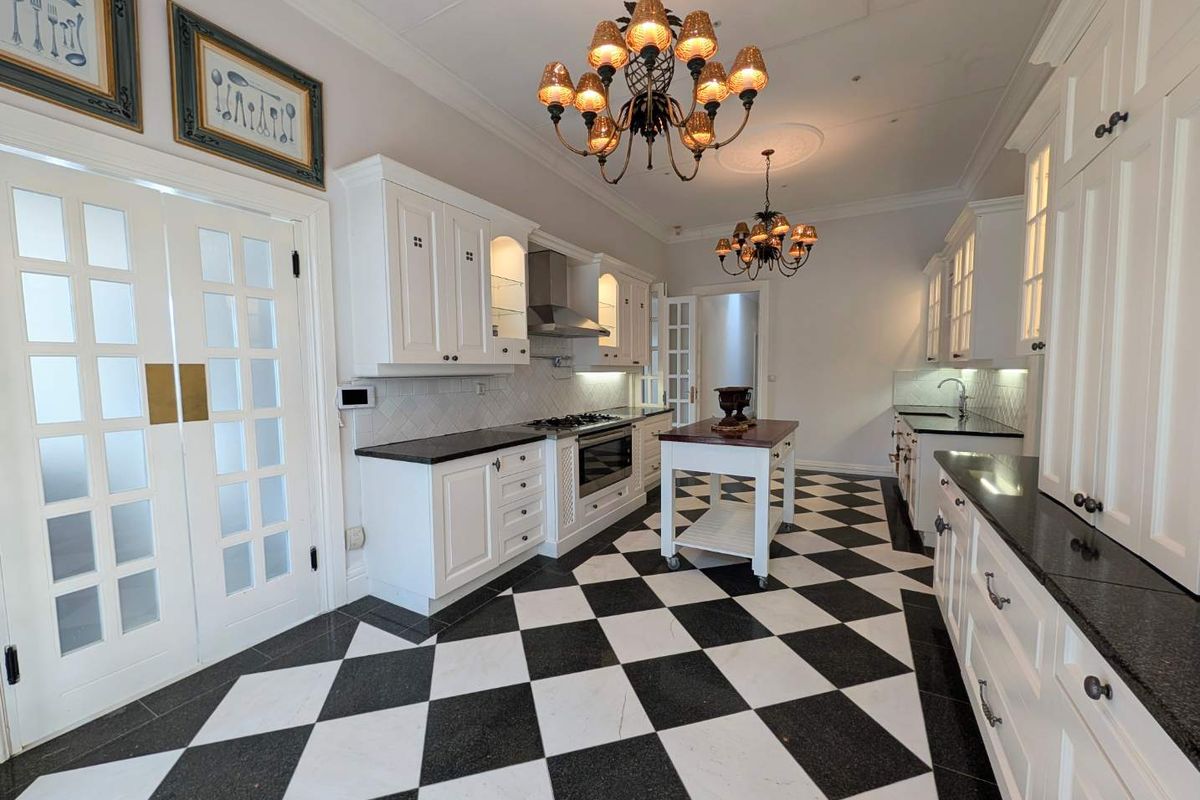 Spacious kitchen featuring classic white cabinetry, black granite countertops, a central island, and striking black and white checkered marble flooring.