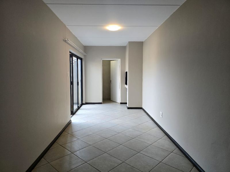 A bright, empty living area featuring neutral walls, tiled flooring, and sliding glass doors that provide access to the exterior.