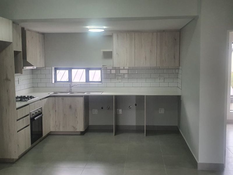 Modern kitchen featuring light wood-grain cabinetry, subway tile backsplash, built-in gas hob, electric oven, and tiled flooring in an open-plan layout.