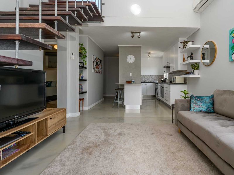 Modern open-plan living area featuring polished concrete floors, a striking open-tread staircase, and a functional kitchen with built-in cabinetry and island.