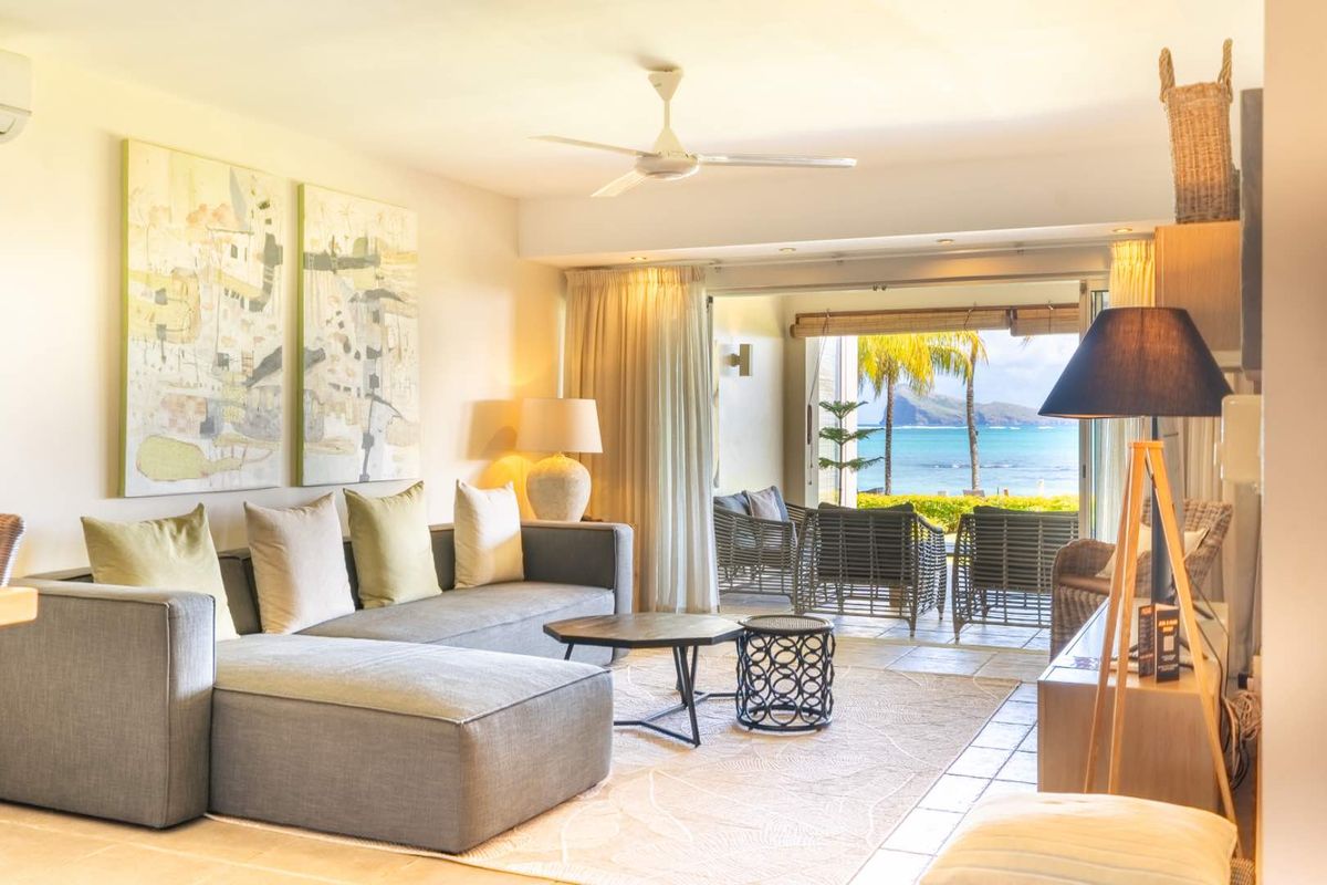 Bright and airy living room featuring tiled flooring, a ceiling fan, and large sliding glass doors opening onto a scenic patio with ocean views.