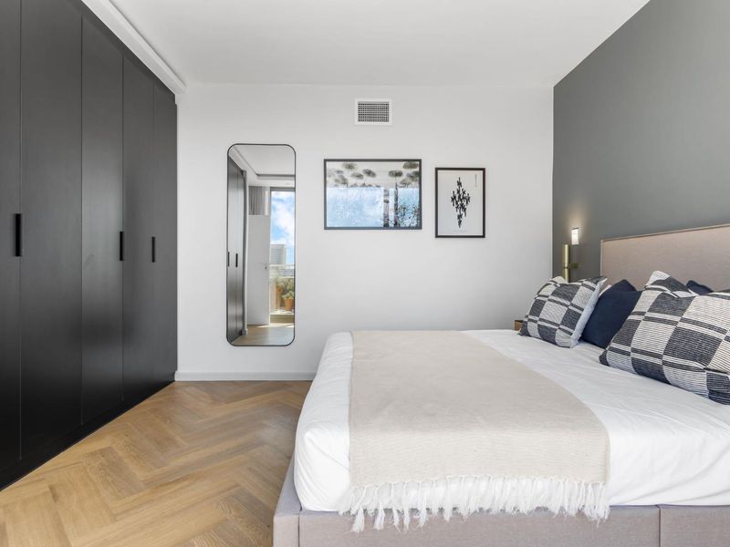 Modern bedroom featuring high-quality herringbone timber flooring, a sleek floor-to-ceiling black built-in wardrobe, and a contemporary grey accent wall.