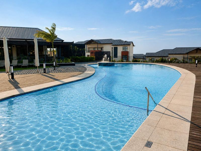 A well-maintained communal swimming pool area featuring a central water fountain, paved surround, and timber decking within a residential estate setting.