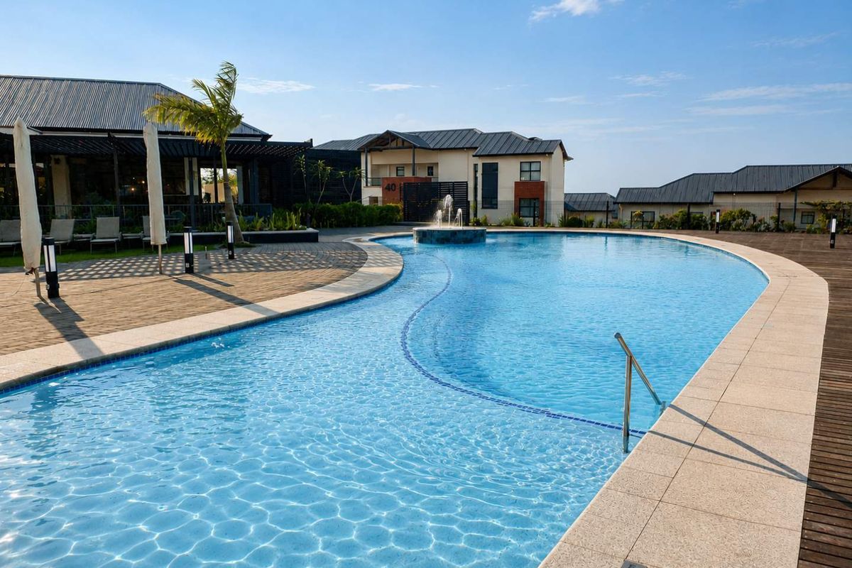 A well-maintained communal swimming pool area featuring a central water fountain, paved surround, and timber decking within a residential estate setting.